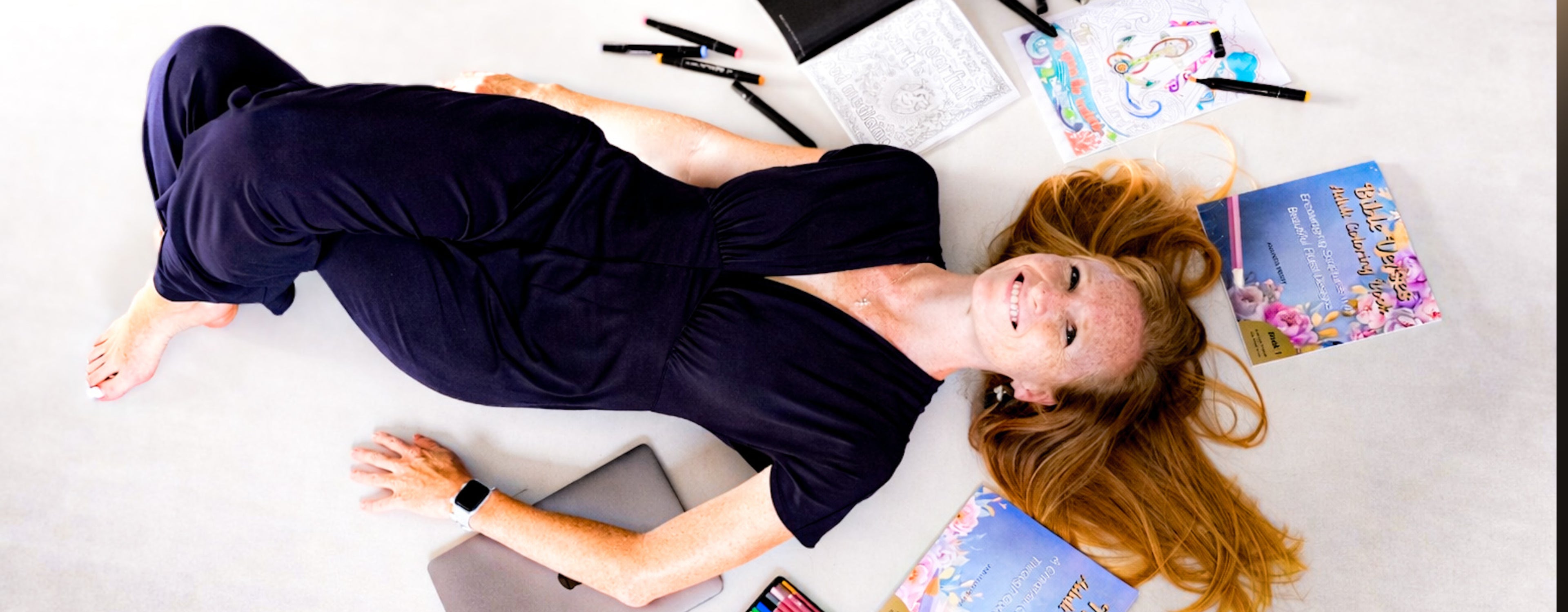 Amanda Perry lying on her book series with a smile on her face wearing a black dress